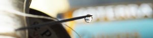 Nähnadel mit Wassertropfen, im Hintergrund Ölfläschchen und Zwirnspule