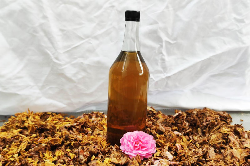Flasche mit selbstgemachtem Rosen-Hydrolat mit Rosenblüte auf getrockneten Rosenblättern